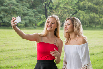 Two female friends taking selfie self portrait photos on smartphone.