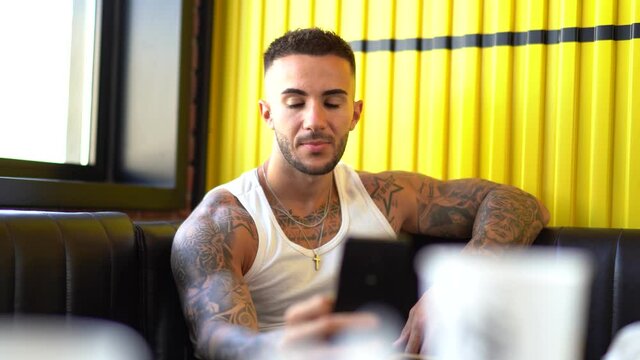 Chico joven tatuado en restaurante tomando un refresco