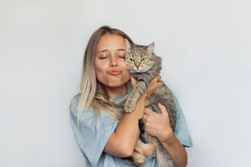 A young beautiful blonde woman with her eye closed holds young Tabby cat in her hands and sends an...
