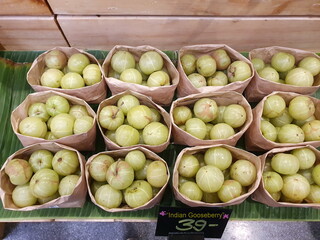 Indian Gooseberry, greenish yellow orbs packed in brown paper bags arranged on wooden trays with...
