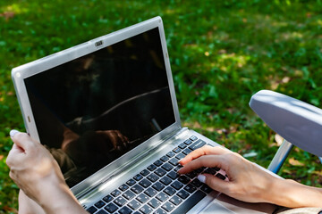 laptop lying on the lap of a girl sitting in a chair in the park