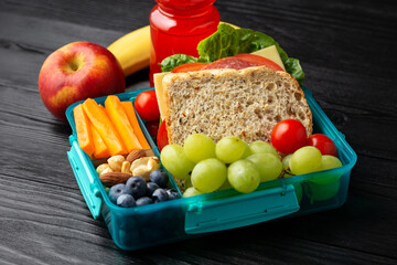 Healthy school, work lunch box with sandwiches and fresh vegetables, nuts, bottle of juicy and fruits on wooden table