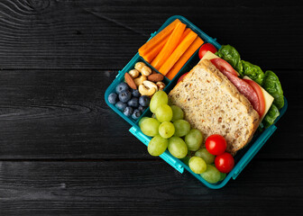 Healthy school, work lunch box with sandwiches and fresh vegetables, nuts and fruits on wooden table