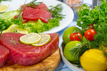 Raw tuna fillet steak with dill, lemon and spices in olive cutting board, ready for cooking