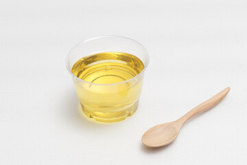 Yellow vegetable oil in a transparent bowl with a wooden spoon on a white background.