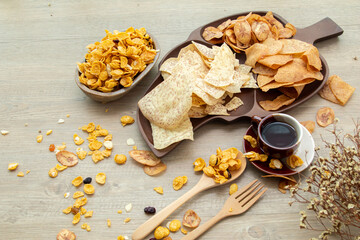 Asian sweet and salty snacks, tasty mixed cornflakes, fried banana and fried taro, nut, grape, and caramel on wooden background natural light. sweet snacks with a cup of tea and copy space