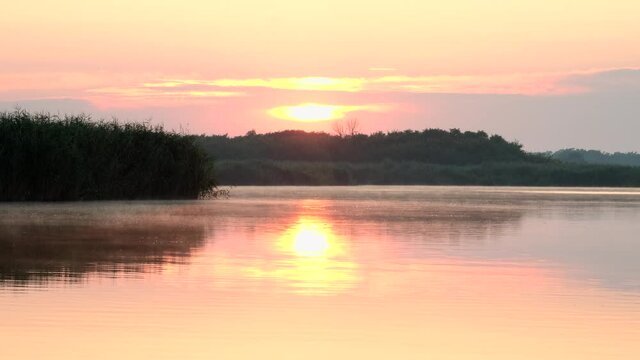 Sunrise over lake and beautiful morning landscape. Morning sun breaks through the thick fog. Early morning on calm river with fog.  Fantastic foggy river in the golden sunlight on water surface