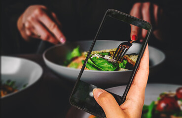 woman hand holding and showing smart phone takes a photo woman eating healthy salad from bowl sitting in cafe. food photos