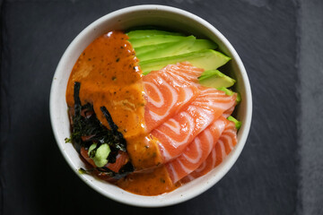 Salmon poke bowl with avocado and seaweed spicy sauce Japanese style. Top view on black table background. Asian trendy food.