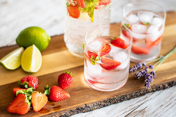 Fresh drink with strawberry and lime placed on wooden desk. Glasses with lemonade and ice. Summer drink.