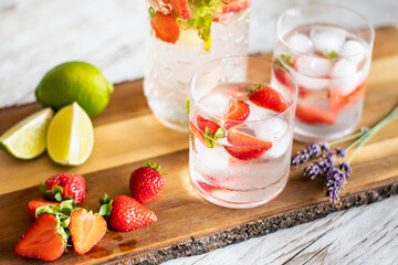 Fresh drink with strawberry and lime placed on wooden desk. Glasses with lemonade and ice. Summer drink.