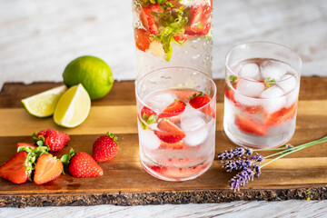 Fresh drink with strawberry and lime placed on wooden desk. Glasses with lemonade and ice. Summer drink.