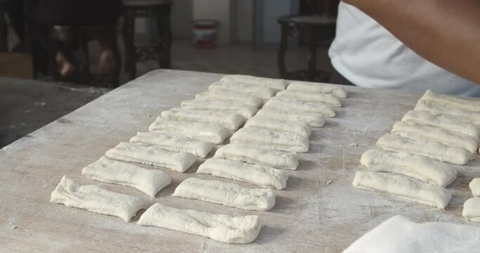 handheld 4K 25fps video of Chef is shaping dough sticks prepare to fry in hot oil.Youtiao is a hugely popular Chinese street food, a deep-fried breadstick crispy outside with a spongy interior.