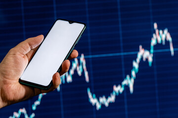 Mockup image of a smartphone with the blank white screen in a hand and stock chart on the background.