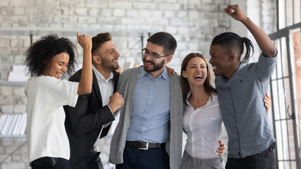 Overjoyed young multiethnic businesspeople have fun celebrate shared business success or victory in...