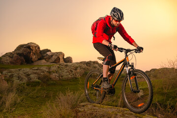 Fototapeta na wymiar Cyclist in Red Riding Bike on the Spring Rocky Trail at Sunset. Extreme Sport and Enduro Biking Concept.