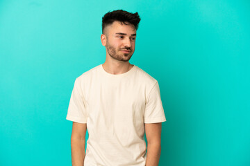 Young caucasian man isolated on blue background having doubts while looking side
