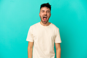 Young caucasian man isolated on blue background shouting to the front with mouth wide open