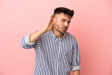 Obraz premium Young caucasian man isolated on pink background listening to something by putting hand on the ear