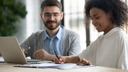 Close up of smiling young African American female employee sign document close deal with male business partner at office meeting. Happy ethnic woman put signature on paperwork make agreement.