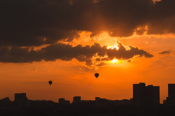 Hot air balloons over the modern city at sunset time.