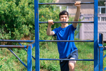 Obraz premium teenage boy exercising outdoors, sports ground in the yard, he posing at the horizontal bar, healthy lifestyle