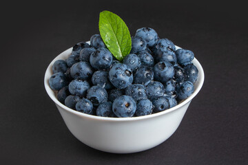 Blueberry with leaves water drops in bowl on dark background