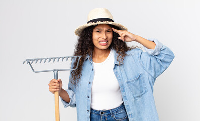 hispanic pretty woman feeling confused and puzzled, showing you are insane wearing a hat and...