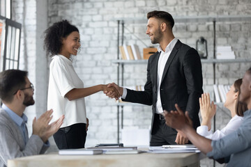 Smiling Caucasian businessman shake hand of excited African American employee congratulate with job success at team meeting. Happy male boss handshake biracial colleague greet with promotion.