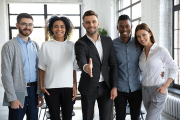 Obraz premium Portrait of overjoyed young multiethnic businesspeople meet newcomer into international team in office. Smiling businessman with multiracial employees stretch hand for handshake. Employment concept.