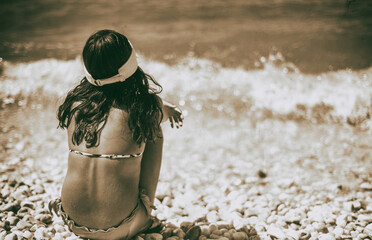 Back view of a girl seated on the beach looking to the sea. Vacation concept.
