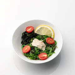 Seaweed salad with cherry tomatoes and lemon. Bowl of asian food isolated on white background. Pan-Asian cuisine. Soft focus.