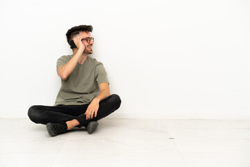 Young caucasian man sitting on the floor isolated on white background keeping a conversation with the mobile phone with someone