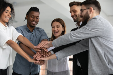 Overjoyed young multiracial diverse colleagues coworkers join stack hands celebrate business shared...