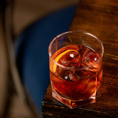 Golden whiskey with ice and lemon in glass on wooden table. Expensive alcoholic shot. Copy space. Soft focus.