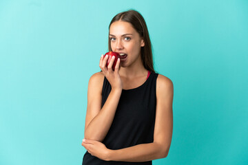 Young woman over isolated blue background eating an apple