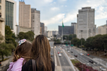 Fototapeta na wymiar Mae e filha observando a cidade de São Paulo. Pessoas em primeiro plano e fundo desfocado. 