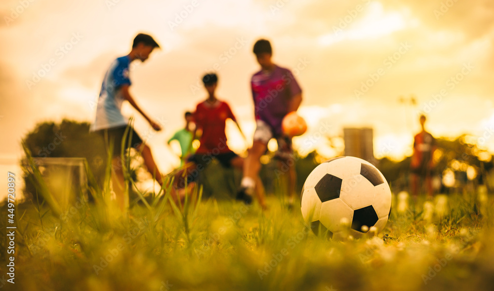 Wall mural Action sport outdoors of kids having fun playing soccer football for exercise in community rural area under the twilight sunset sky