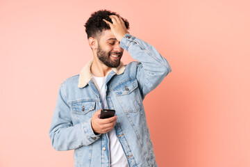 Young Moroccan man using mobile phone isolated on pink background has realized something and...