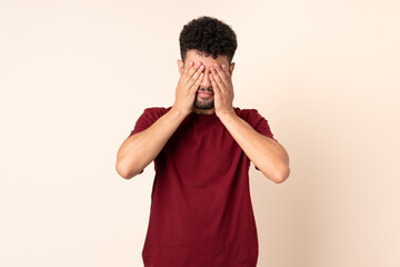 Young Moroccan man isolated on beige background covering eyes by hands