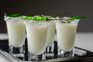 Coconut cocktail in drink shot glass decorated with coconut flakes and green bird eye chilli served on a silver tray