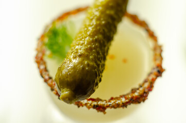 Close up of a drink based on vodka and cucumber juice in a shot glass decorated with small pickled cucumber and dill