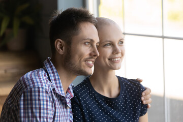Happy young man and hairless ill woman looking out of window with hope for remission, smiling at...