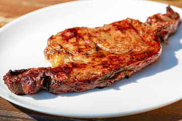 Beef steak on a white plate. The plate is on a wooden table. Selective focus