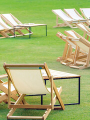 Many empty white deck chairs with tables in lawn is surrounded by shady green grass. Comfortable on...