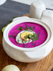 Close-up of cold chlodnik soup on a wooden board. Soup of Polish Belarusian and Russian cuisine made of beetroot and kefir, decorated with half an egg. Healthy food