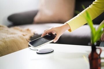 Charging mobile phone battery with wireless charging device in the table. Smartphone charging on a charging pad. Mobile phone near wireless charger Modern lifestyle technology concept. - obrazy, fototapety, plakaty