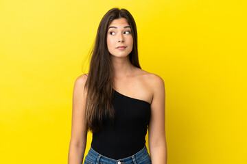 Young Brazilian woman isolated on yellow background making doubts gesture looking side