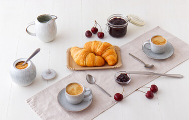 Tasty healthy food, breakfast, brunch or just snacks. Freshly baked croissants with jam from latest cherry harvest and fresh espresso. White wooden table background.