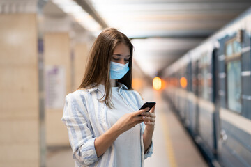 Young caucasian woman wear protective face mask, using mobile smart phone, chatting in social...